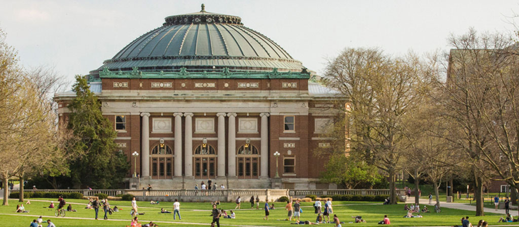 Foellinger Auditorium at the University of Illinois on a spring day. Students are relaxing on the grass.